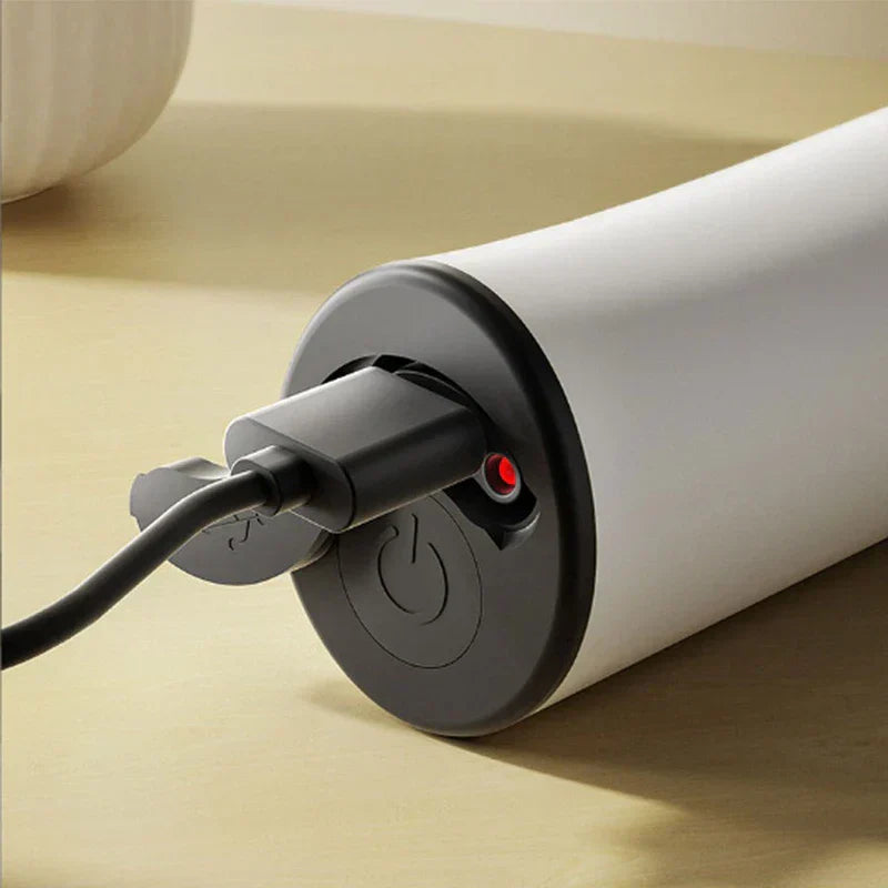varita espumadora - Primer plano de un cable de carga USB conectado a un dispositivo cilíndrico blanco, con luz indicadora roja y botón de encendido en su tapa final negra