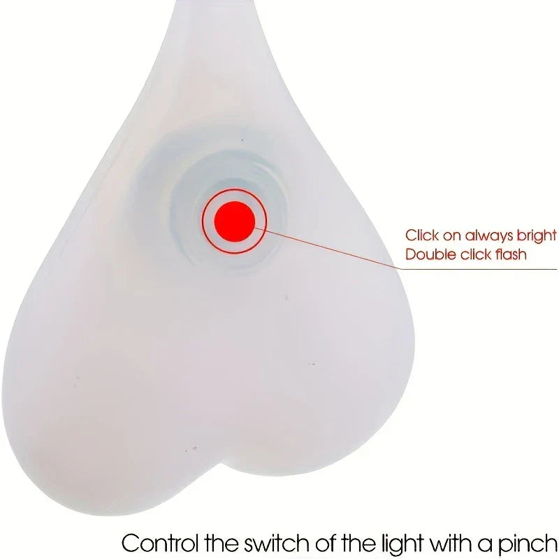 luz trasera de bicicleta con led a pilas - primer plano de una luz de silicona con forma de corazón con botón central rojo, y texto que indica clic para luz constante, doble clic para destello y pellizco para controlar