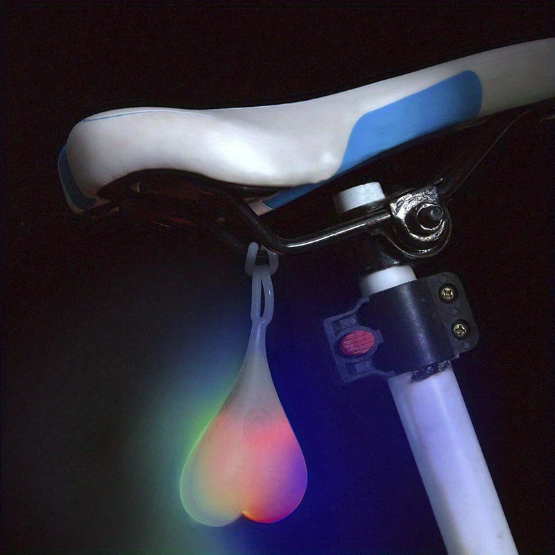 Led Bike Tail Rear Light - Colorful glowing teardrop-shaped light hangs from a white and blue bicycle seat in dark surroundings