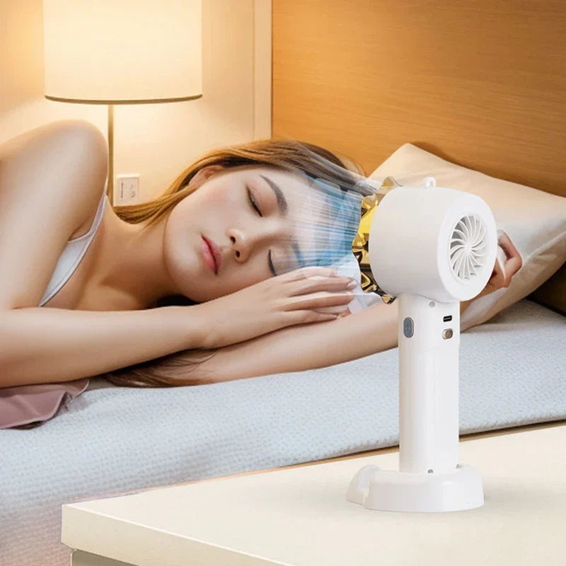 Personal Cooling Fan - A woman lies on a bed while a white handheld fan with gold accent sits on a bedside table, blowing air toward her face.