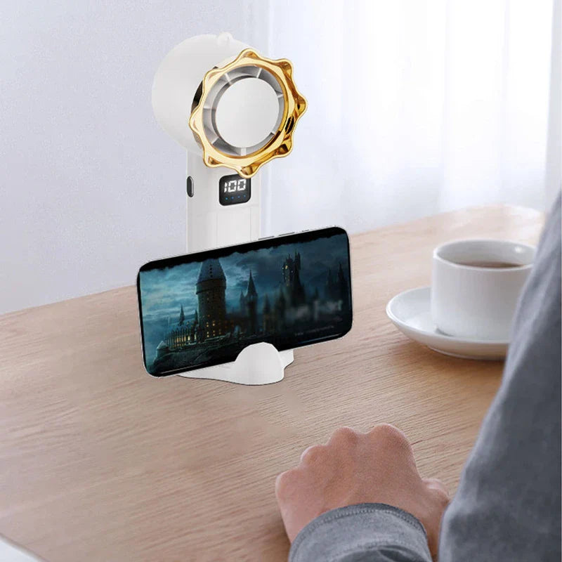 persönlicher kühlventilator - Ein weißer Handventilator mit goldener Verzierung steht auf einem Holztisch, seine Basis hält ein Smartphone mit einer Schloss-Szene, daneben eine Kaffeetasse