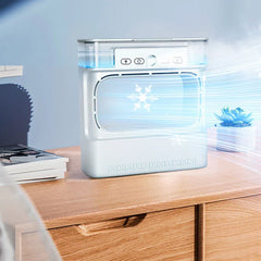 Desktop air cooler humidifier sits on a wooden desk, emitting cool airflow, with stacked magazines and a small succulent pot nearby.