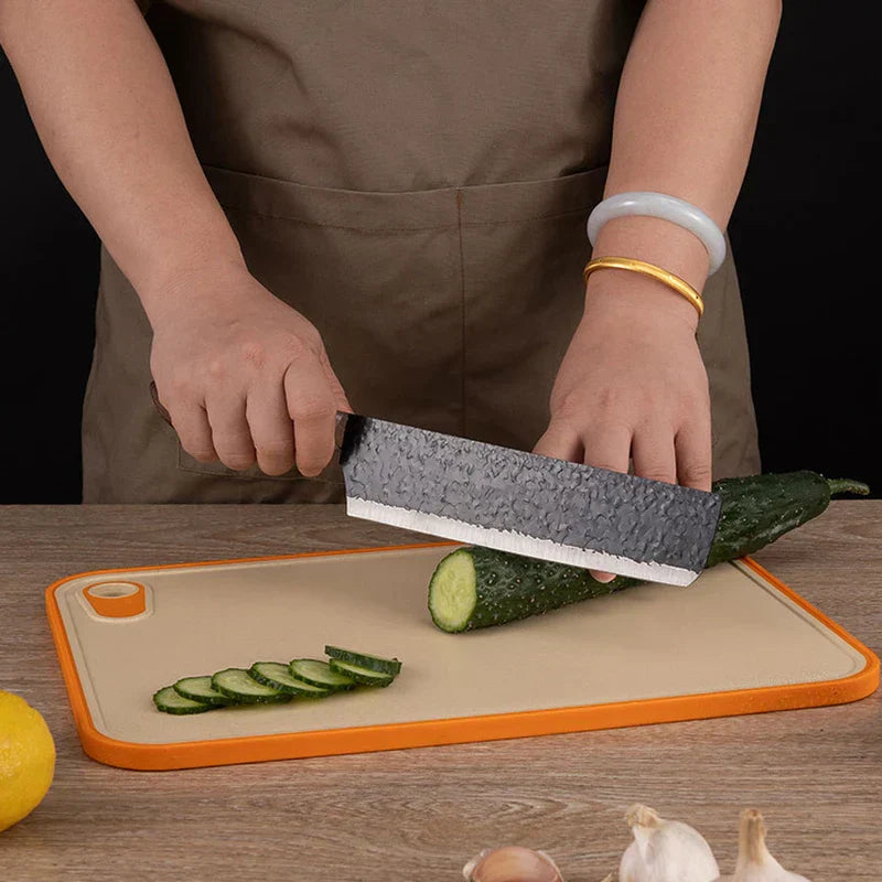 Hammered Knife Set - Person slicing a cucumber on an orange-rimmed cutting board with a wide hammered kitchen knife