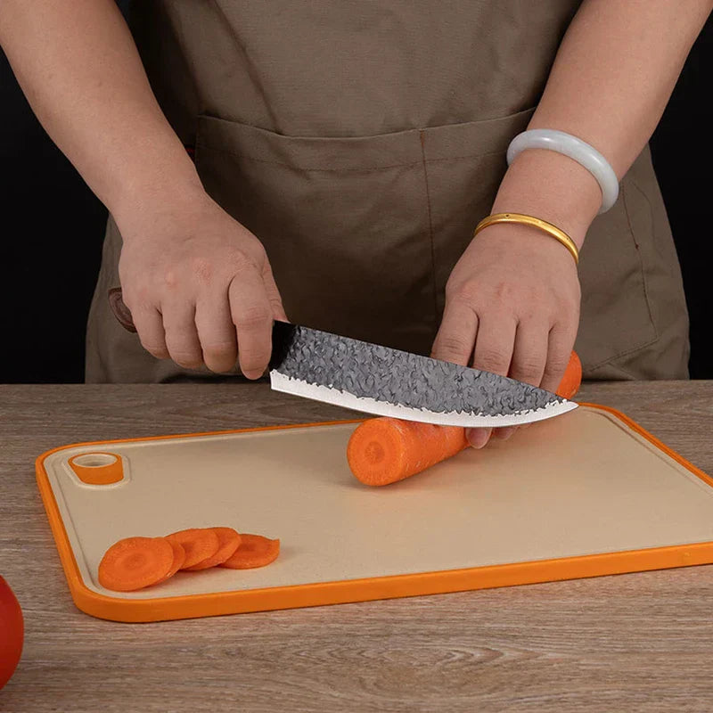 Hammered Knife Set - Person slicing a carrot on an orange-rimmed cutting board with a curved hammered kitchen knife