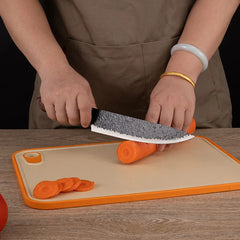 Hammered Knife Set - Person slicing a carrot on an orange-rimmed cutting board with a curved hammered kitchen knife
