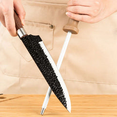 Hammered Knife Set - Hands hold a hammered blade knife and a honing rod crossed over a wooden cutting board, with an apron in the background.