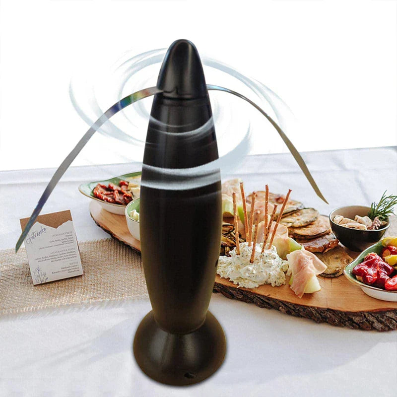 Fly Repellent Fan Device - Black blade-spinning device on a white table, with a wooden charcuterie board of assorted foods behind it