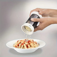 Butter Grater - Two hands hold a cylindrical cheese grinder, sprinkling shredded cheese over a plate of pasta.