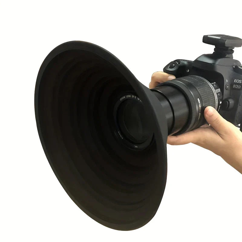 parasol para lente de cámara - Una mano sostiene una cámara DSLR equipada con un gran parasol de lente negro en forma de embudo sobre un fondo blanco.