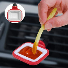 A hand dips a french fry into ketchup in a red and white car vent sauce holder clipped to a car air vent.