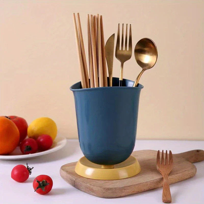 Soporte cerámico para palillos, escurridor y organizador de cubiertos - Un organizador de cubiertos azul con base amarilla sostiene palillos de madera y cubiertos dorados, sobre una tabla de madera, con tomates cherry y fruta en un plato cerca.