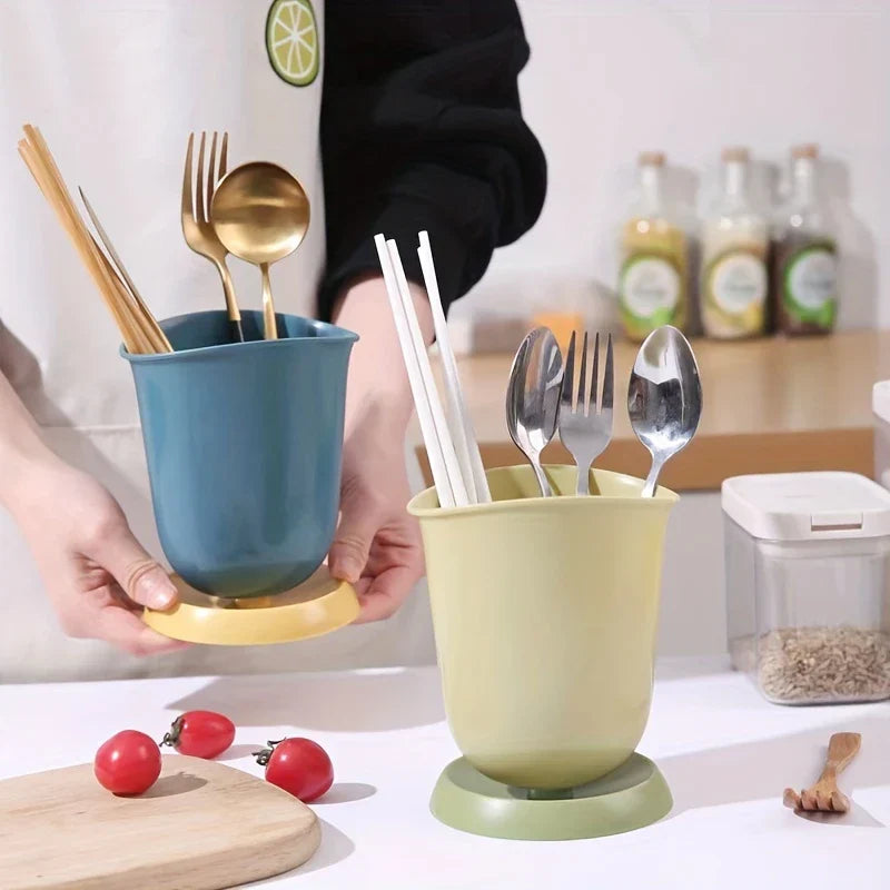 Soporte cerámico para palillos, escurridor y organizador de cubiertos - Dos organizadores de cubiertos con palillos y cubiertos planos descansan sobre una encimera; una persona sostiene el azul y amarillo. Cerca hay tomates cherry y un pequeño tenedor de madera.