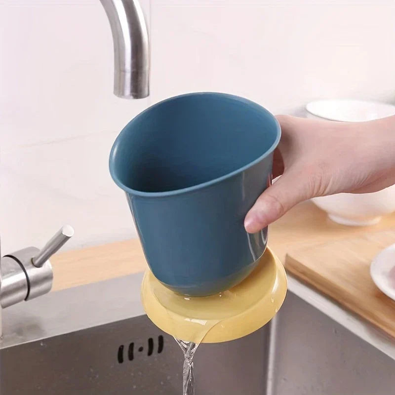 Soporte cerámico para palillos, escurridor y organizador de cubiertos - Una mano sostiene un vaso organizador azul sobre un fregadero; el agua escurre de su base amarilla hacia el fregadero de abajo.