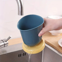 Soporte cerámico para palillos, escurridor y organizador de cubiertos - Una mano sostiene un vaso organizador azul sobre un fregadero; el agua escurre de su base amarilla hacia el fregadero de abajo.