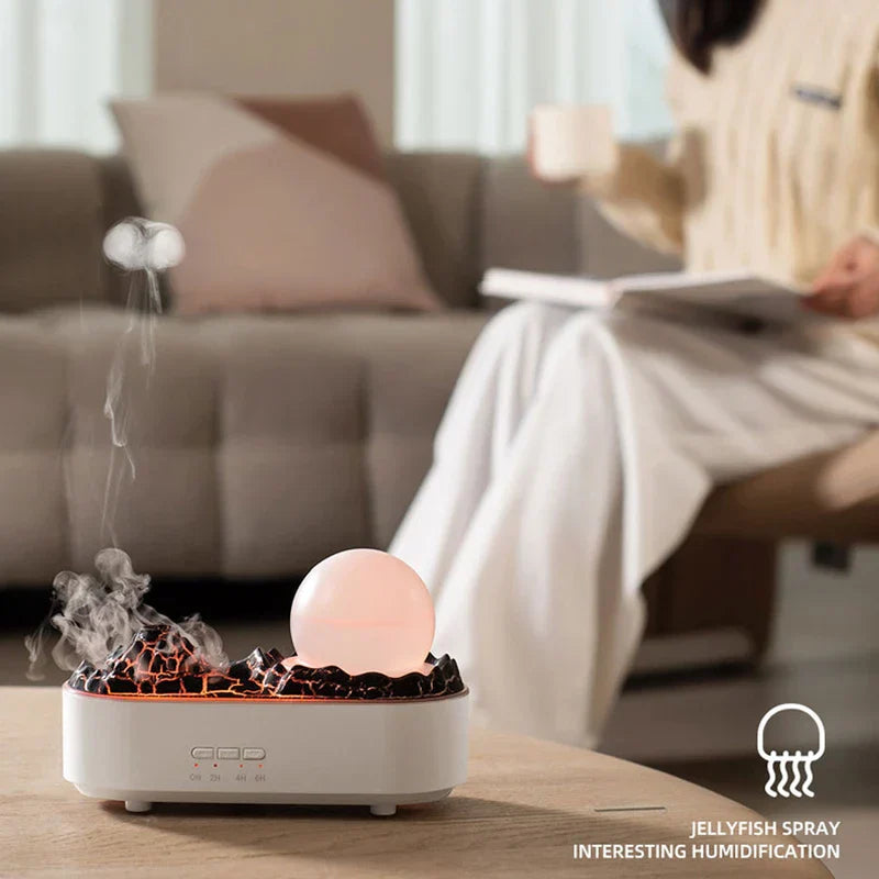 Cool Mist Humidifier - Humidifier with orange lit crackle mountain top, warm lit moon sphere, rising mist, on wood table with a seated person on a couch in the background