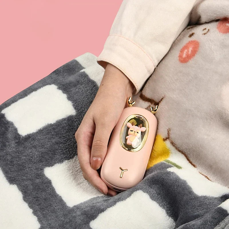 Rechargeable Hand Warmer - A hand holds the light pink deer-designed device resting on a fuzzy checkered blanket