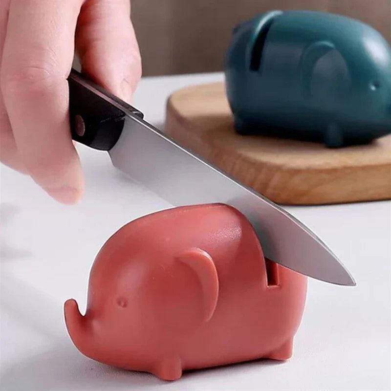 Mini Knife Sharpener - Hand pulling a kitchen knife through the rose colored sharpener, teal variant resting on a wooden cutting board in background