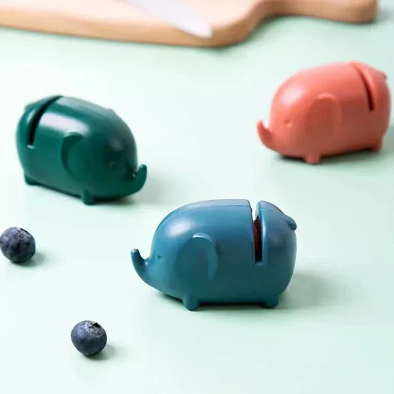 Mini Knife Sharpener - Three small elephant-shaped objects in teal, dark green and coral sit on a pale green surface with two blueberries nearby