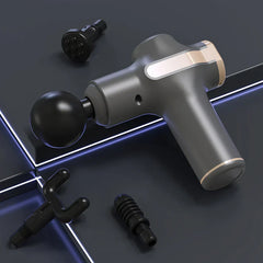 Grey mini massage gun with spherical massage head attached, three other massage heads placed nearby on a dark surface with light lines
