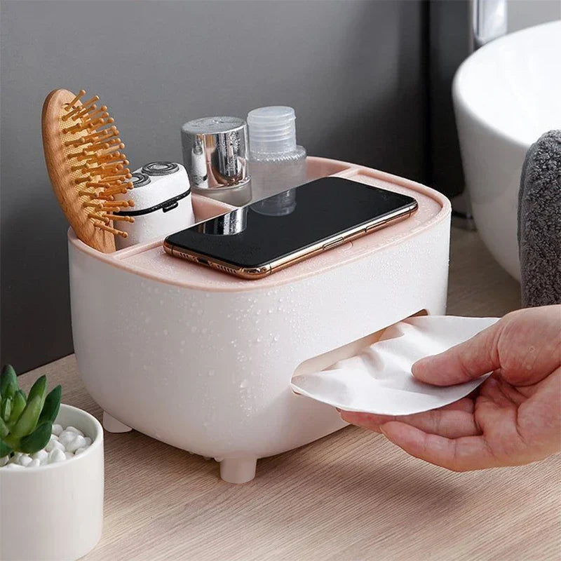 A desktop organizer shelf with tissue box holder sits on a bathroom counter, holding a hairbrush, toiletries, and a phone, as a hand pulls a tissue from it.