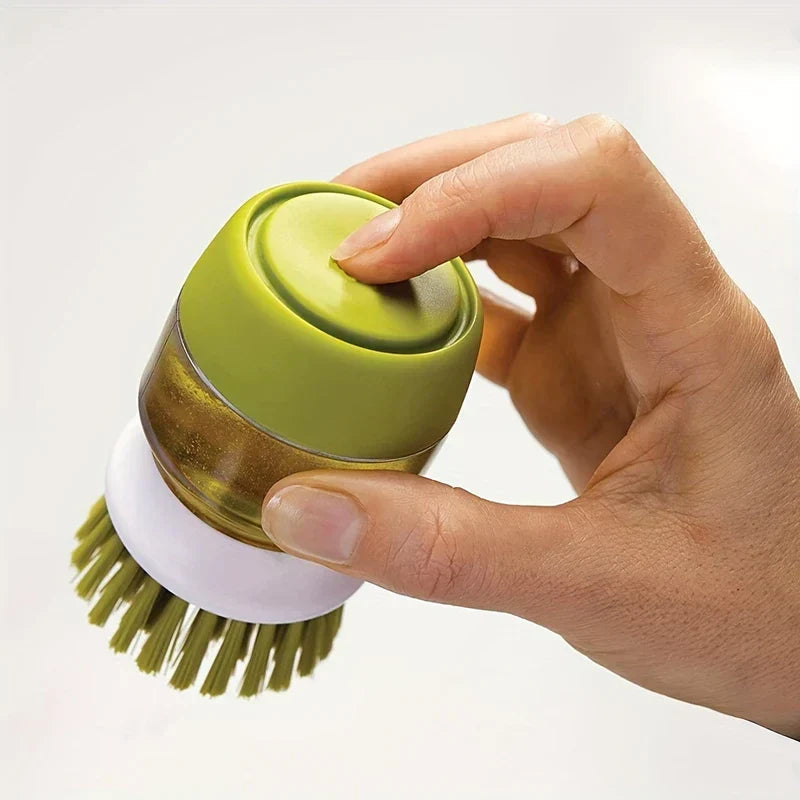Gros plan d'une main tenant une brosse à vaisselle à paume avec distributeur de savon, le pouce sur son bouton de pression supérieur