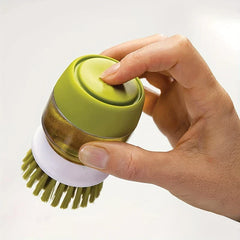 Gros plan d'une main tenant une brosse à vaisselle à paume avec distributeur de savon, le pouce sur son bouton de pression supérieur