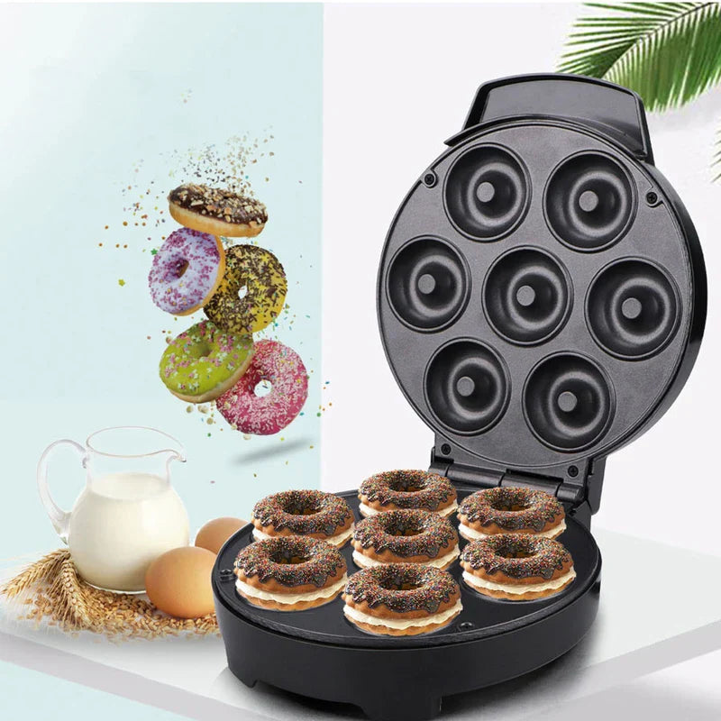 Mini Donut Maker - Open black donut maker with seven donuts on its cooking surface, shown with eggs, milk pitcher, and decorated donuts nearby.
