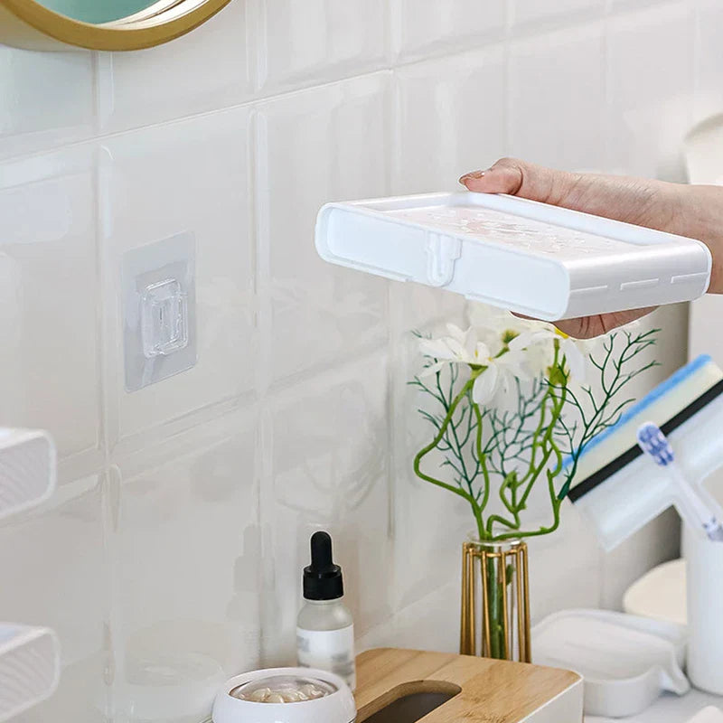 Soap Dish Holder - A hand holds a white wall-mounted soap tray near a clear adhesive hook attached to a white tiled bathroom wall.