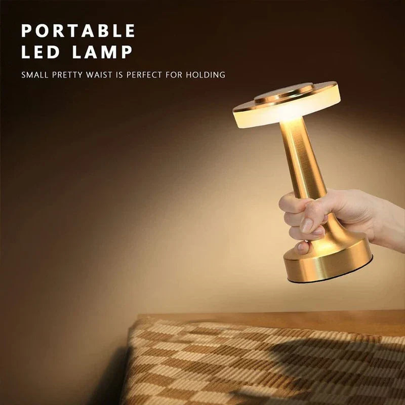 Led Desk Lamp - Hand gripping the tapered middle of a lit brass-toned portable table lamp