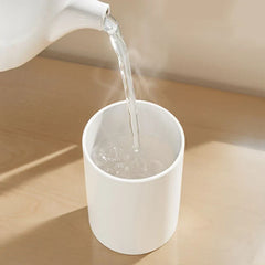 Cup Holder Set - Hot water pouring from a kettle into a white cylindrical cup on a light wood surface