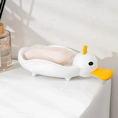 Duck Soap Dish Holder - Duck-shaped dish holding a pale pink bar of soap, placed on a white countertop next to a clear glass bottle