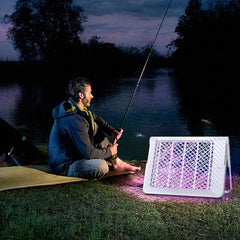 Racket Mosquito - Mosquito lamp placed on grass near a man fishing by a riverside at dusk.