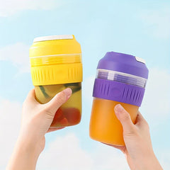 Electric Citrus Juicer - Two hands holding yellow and purple juicer units, one filled with orange juice and one with infused fruit water