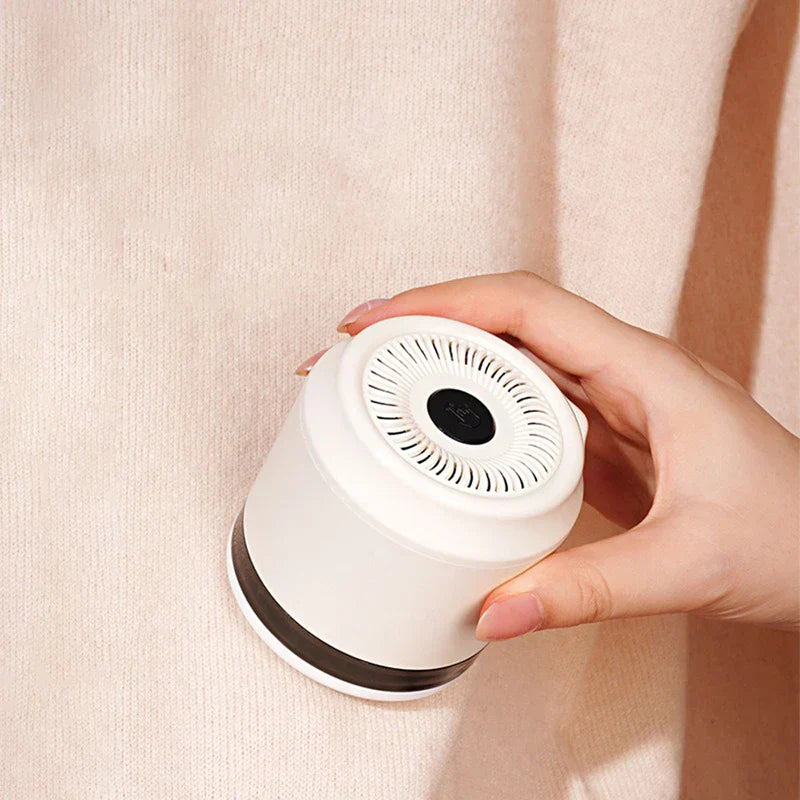 Lint Remover - A hand holds a white fabric shaver against a knit sweater surface.