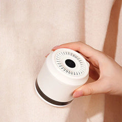Lint Remover - A hand holds a white fabric shaver against a knit sweater surface.