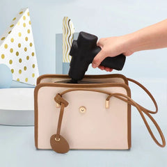 Electric Fascia Vibration Recovery Gun - Hand placing a black mini massage gun into an open two-tone beige and tan small crossbody handbag