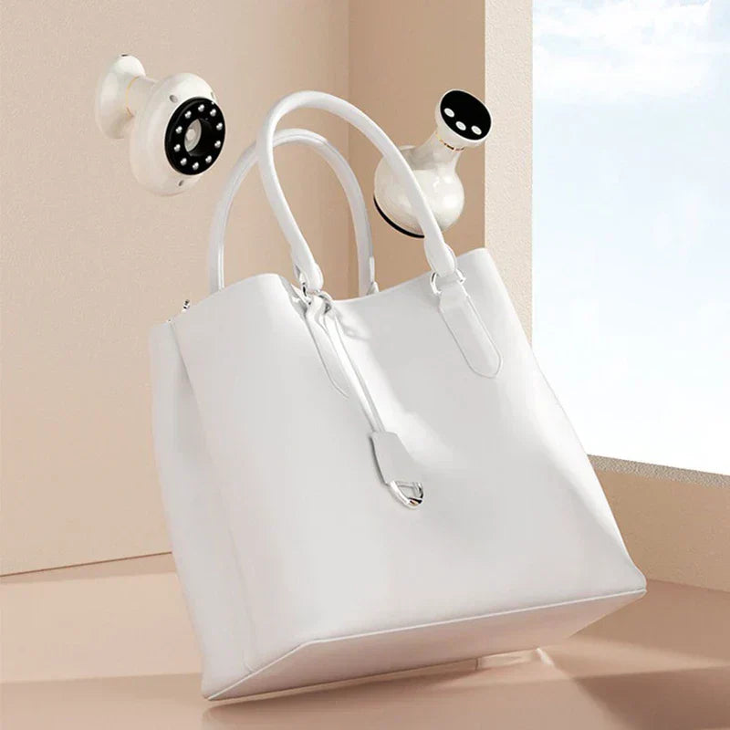 gua sha électrique - Deux appareils portatifs blancs placés à côté d'un sac à main structuré blanc près d'une fenêtre