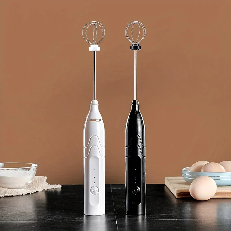 Electric Hand Mixer - White and black handheld electric whisks standing upright on a dark surface, with a bowl of powder and eggs in the background.