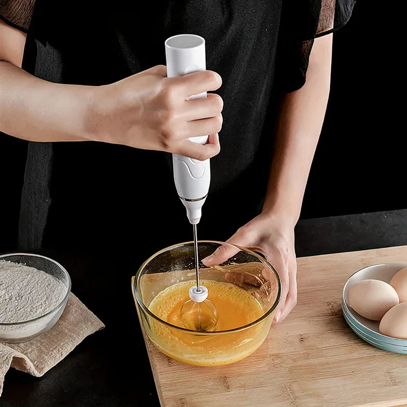 Electric Hand Mixer - Person using a handheld electric mixer to beat eggs in a glass bowl on a wooden countertop