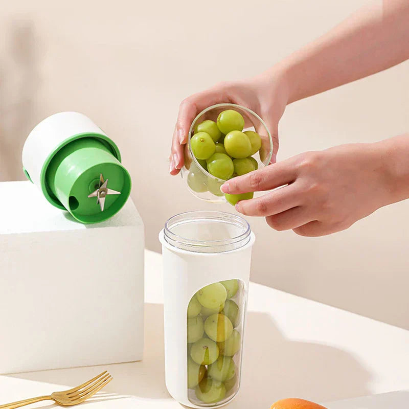 Juicer Extractor Machine - Hands pouring green grapes into a portable blender cup, with its blade lid resting on a white block beside a gold fork and orange.