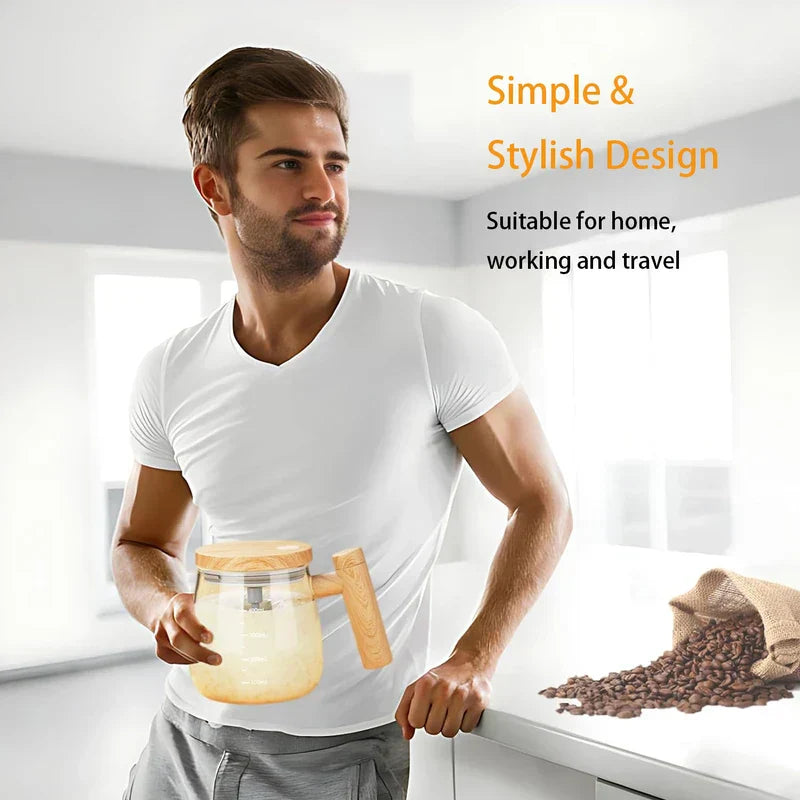 A man in a white shirt holds a glass self-stirring mug with a wooden lid and handle in a bright kitchen, with spilled coffee beans on a counter nearby.