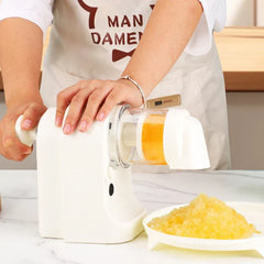 A person turns the side handle of an ice shaver machine, producing yellow shaved ice in a dish