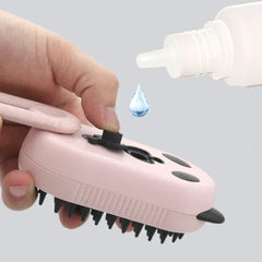 A hand opens the fill port of a pink electric spray handle massage brush, with a drop of liquid falling into it.
