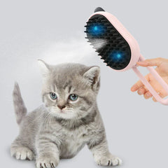 A hand holding a pink electric spray handle massage brush with mist and blue lights, near a sitting gray kitten.