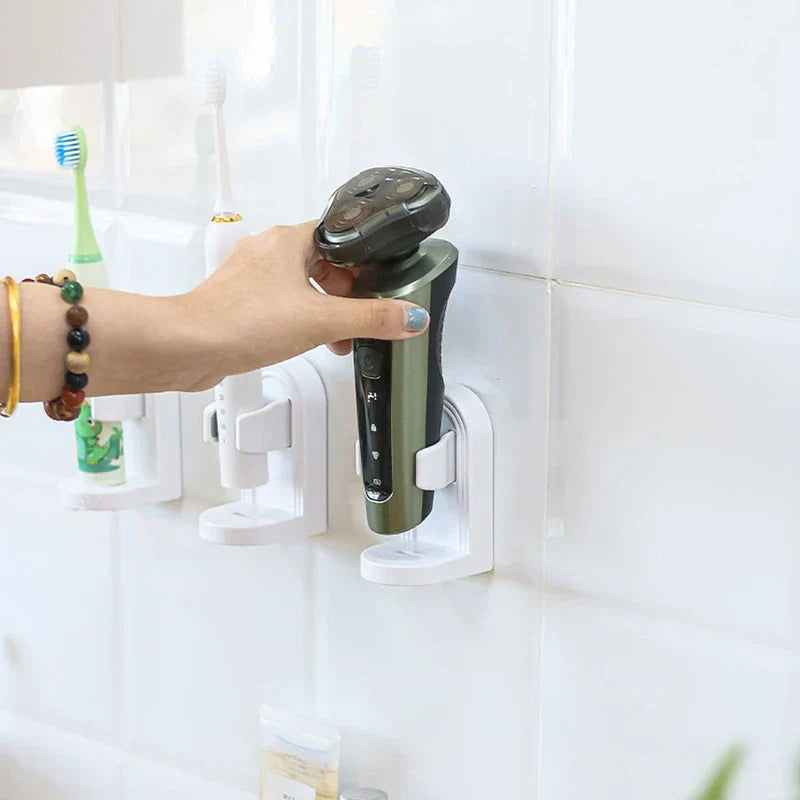Soporte para cepillo de dientes eléctrico - Una mano con pulseras de cuentas sostiene una afeitadora eléctrica colocada en un soporte blanco montado en pared, con dos cepillos de dientes eléctricos en soportes iguales sobre una pared de azulejos