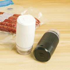 Two handheld electric pumps, white and black, rest on wood with vacuum-sealed food bags visible behind them, showcasing vacuum storage bags with electric pump.