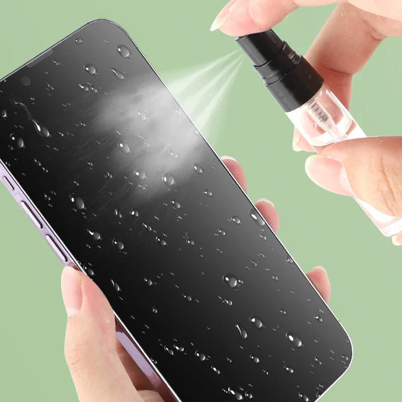 Hands spray liquid from a small clear spray bottle onto a wet black smartphone screen