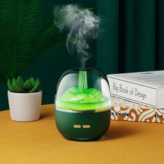 A teal humidifier with green internal lighting emits mist, set on a yellow table with a small succulent at left and stacked books at right