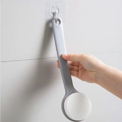 Loofah - Hand hanging a long-handled bath brush on an adhesive wall hook mounted to a tiled bathroom wall