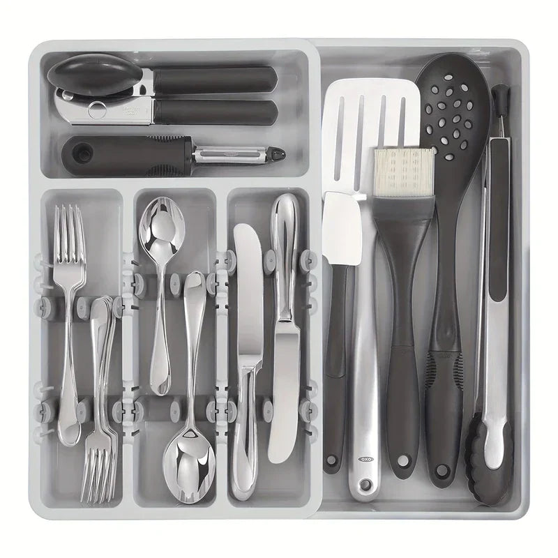 A cutlery drawer organizer holding assorted forks, spoons, knives, and kitchen utensils in separate compartments